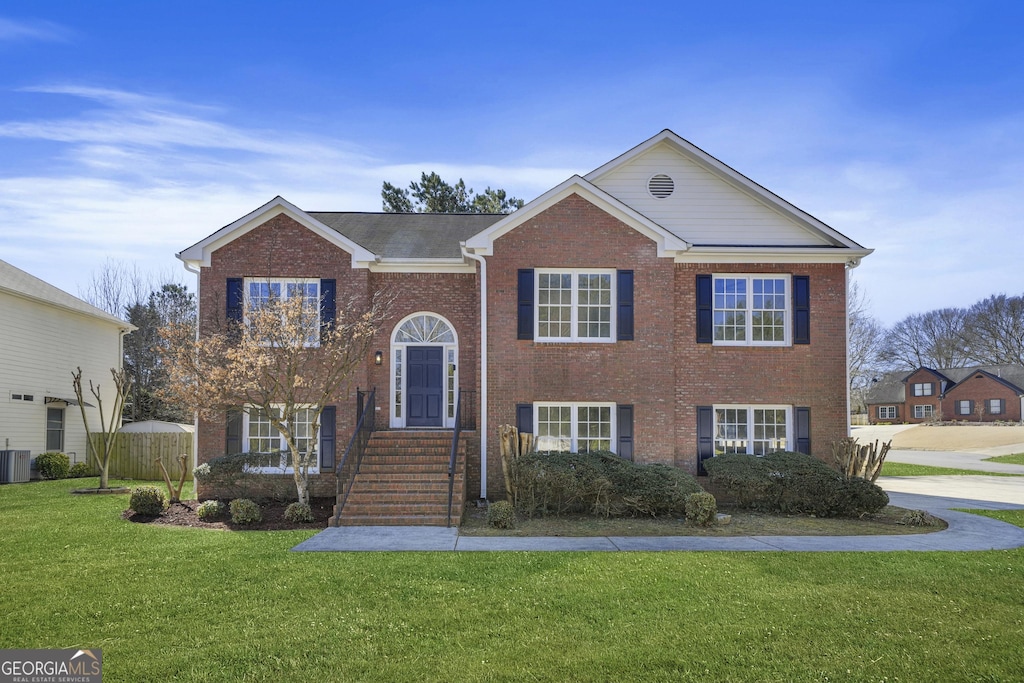 raised ranch with central AC, brick siding, and a front yard