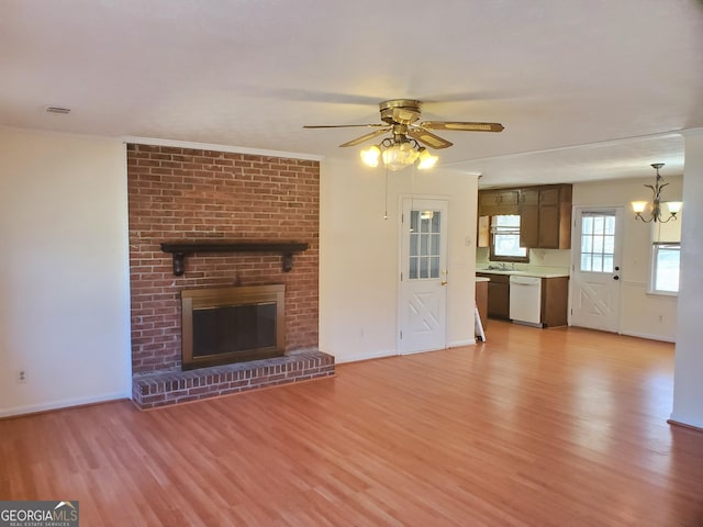 unfurnished living room with baseboards, light wood-style flooring, ornamental molding, a brick fireplace, and ceiling fan with notable chandelier