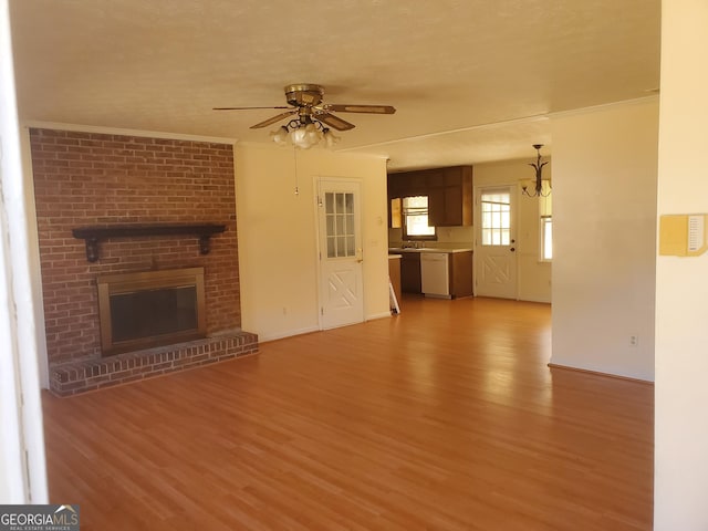 unfurnished living room with a ceiling fan, light wood-type flooring, a brick fireplace, and crown molding