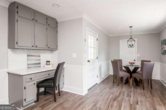 dining room featuring light wood finished floors, a wainscoted wall, a textured ceiling, and ornamental molding