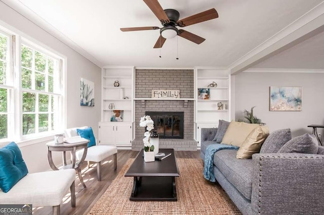 living room featuring built in features, a brick fireplace, wood finished floors, and ornamental molding