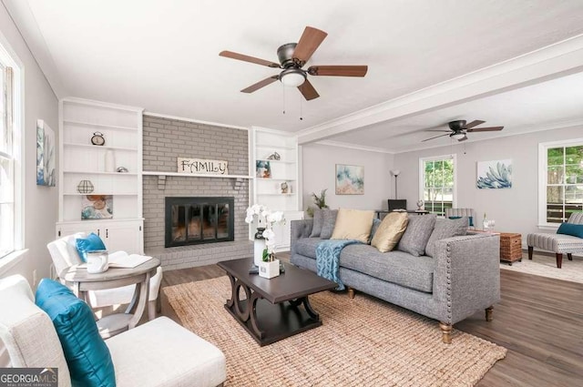 living room featuring a brick fireplace, crown molding, a ceiling fan, and wood finished floors