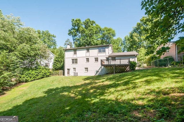 rear view of property featuring a chimney, a lawn, a wooden deck, and fence