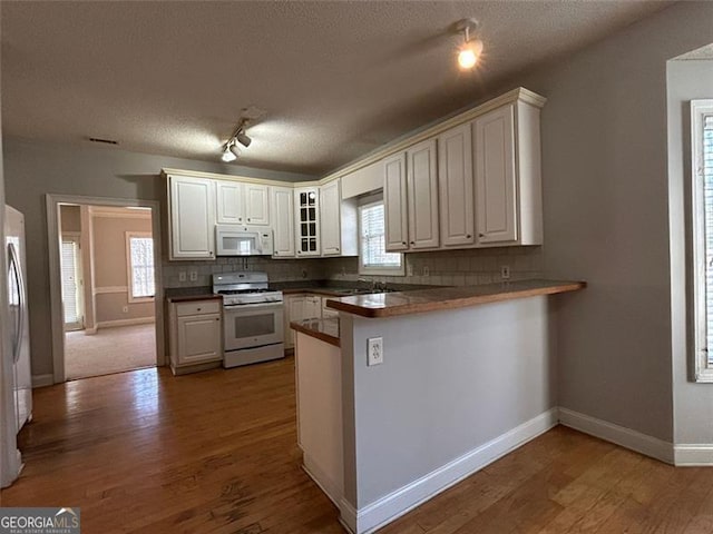 kitchen featuring white appliances, a peninsula, decorative backsplash, and wood finished floors