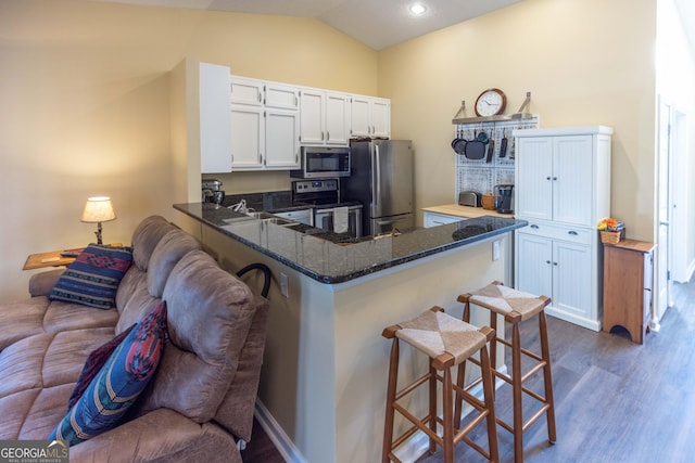 kitchen with appliances with stainless steel finishes, a breakfast bar, dark wood-type flooring, dark stone countertops, and a peninsula