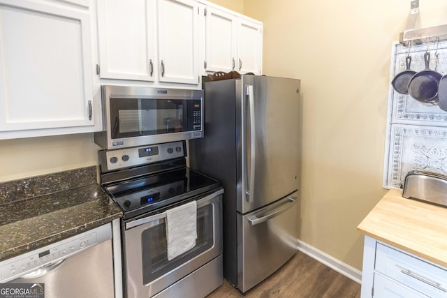 kitchen featuring dark wood-style flooring, stainless steel appliances, white cabinetry, dark stone countertops, and baseboards