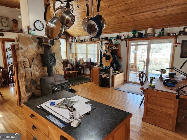 kitchen featuring lofted ceiling, dark countertops, light wood-style floors, wood ceiling, and a wood stove