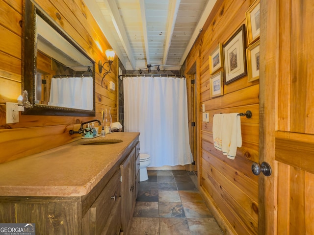 full bath featuring a shower with shower curtain, toilet, stone finish floor, wooden walls, and vanity