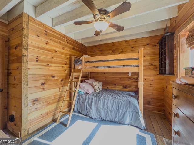 unfurnished bedroom featuring ceiling fan, wooden walls, visible vents, beamed ceiling, and wood-type flooring