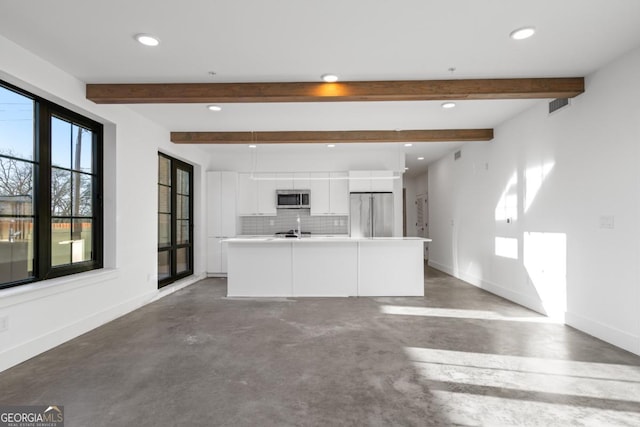 kitchen featuring finished concrete flooring, baseboards, white cabinets, appliances with stainless steel finishes, and backsplash