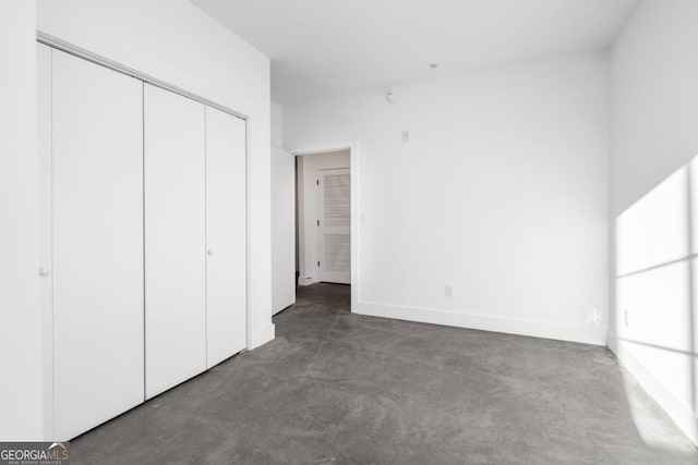 unfurnished bedroom featuring finished concrete flooring, baseboards, and a closet