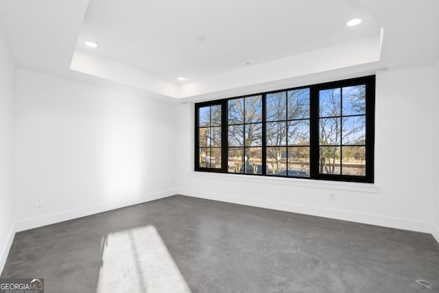 unfurnished room with concrete flooring, a tray ceiling, recessed lighting, and baseboards