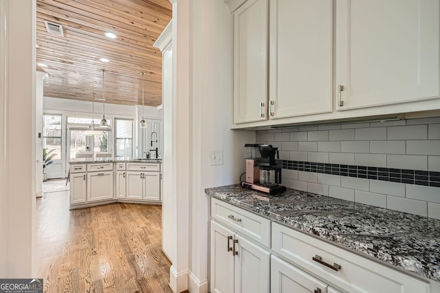 kitchen with decorative backsplash, wooden ceiling, light wood-style flooring, dark stone countertops, and a sink