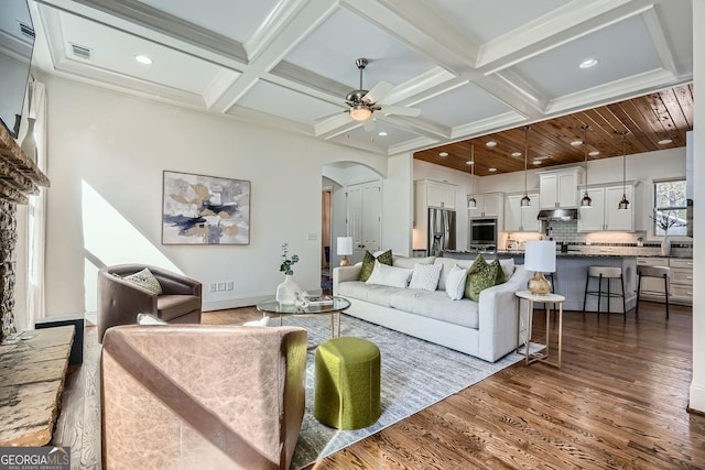 living area featuring arched walkways, coffered ceiling, dark wood-style floors, ceiling fan, and beamed ceiling