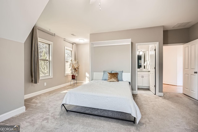 bedroom with baseboards, connected bathroom, and light colored carpet