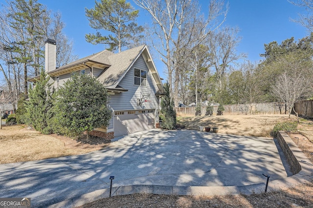 view of side of property featuring a garage, a shingled roof, fence, concrete driveway, and a chimney