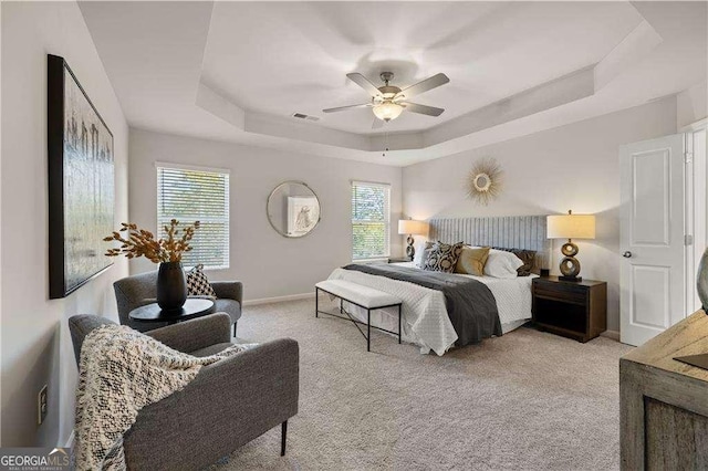 carpeted bedroom featuring visible vents, a tray ceiling, ceiling fan, and baseboards