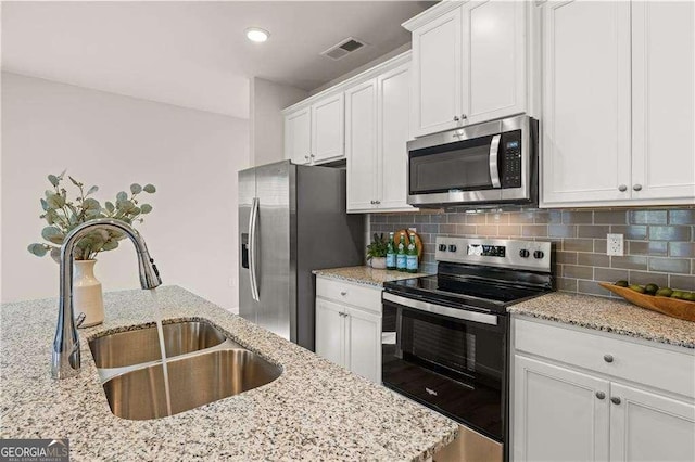 kitchen with appliances with stainless steel finishes, a sink, white cabinetry, and tasteful backsplash