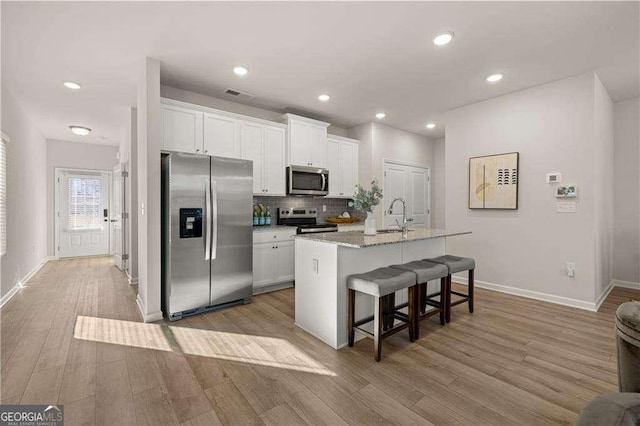 kitchen featuring backsplash, appliances with stainless steel finishes, white cabinetry, light wood-type flooring, and a kitchen breakfast bar