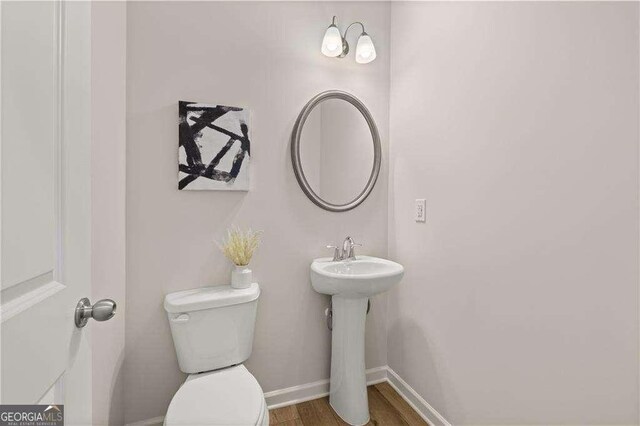 half bathroom with toilet, a sink, baseboards, and wood finished floors