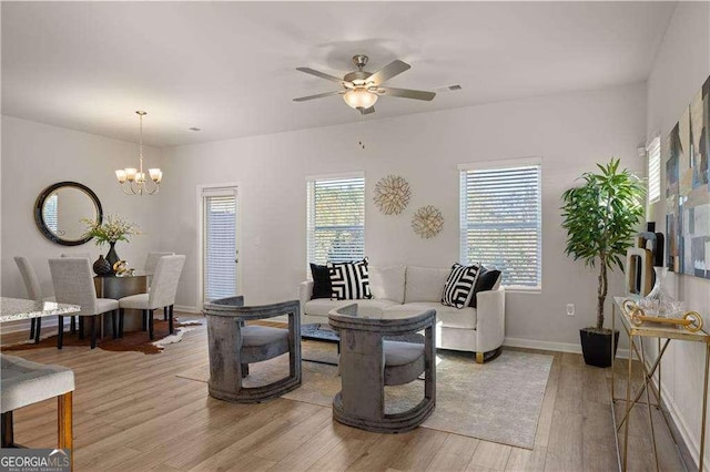 living room with light wood-style floors, baseboards, and ceiling fan with notable chandelier