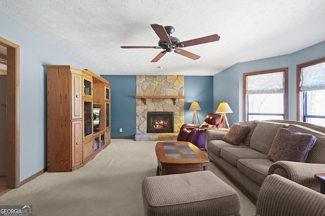 living area featuring baseboards, ceiling fan, light colored carpet, a stone fireplace, and a textured ceiling