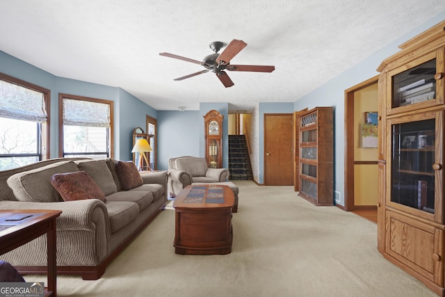 living room featuring stairway, light colored carpet, a textured ceiling, and ceiling fan