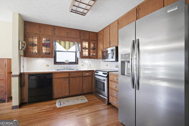 kitchen with light wood finished floors, a sink, stainless steel appliances, light countertops, and brown cabinets