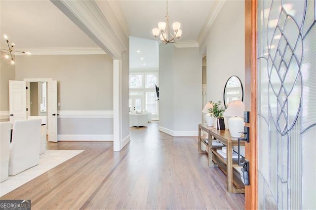 entryway with a chandelier, ornamental molding, light wood finished floors, and baseboards