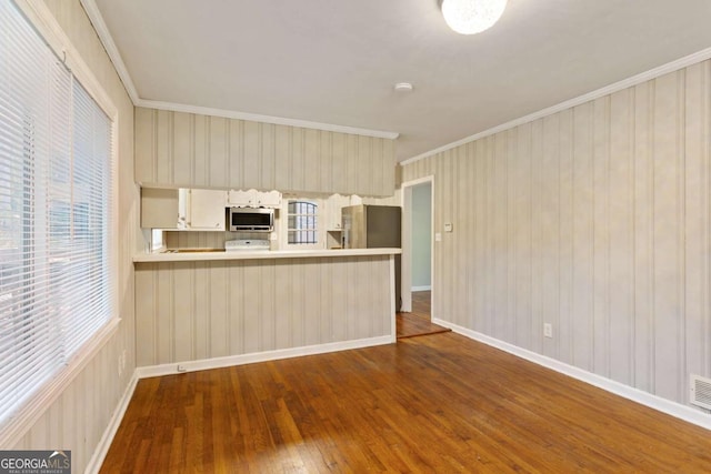 kitchen featuring dark wood finished floors, appliances with stainless steel finishes, a peninsula, light countertops, and crown molding