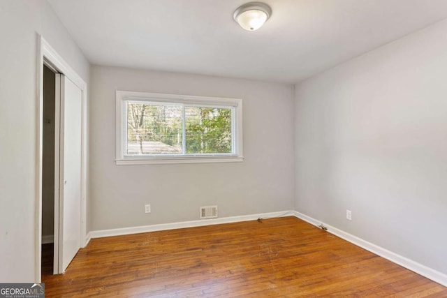 unfurnished bedroom with hardwood / wood-style flooring, baseboards, visible vents, and a closet