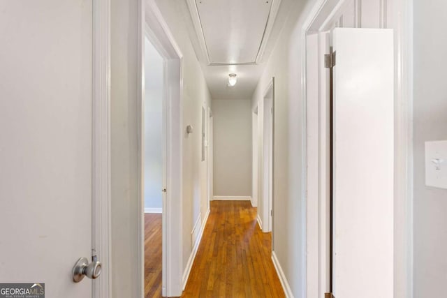 corridor with wood finished floors, attic access, and baseboards