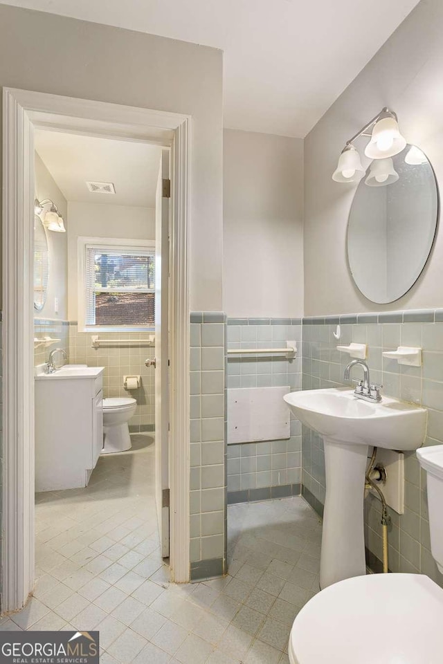 half bath with visible vents, wainscoting, toilet, and tile patterned floors