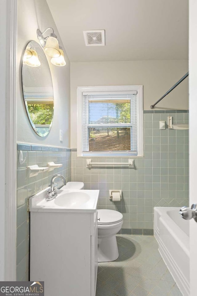 bathroom featuring toilet, vanity, visible vents, tile walls, and tub / shower combination