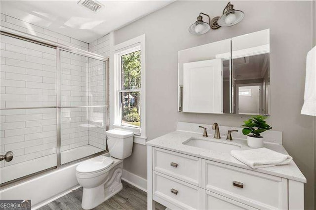 full bath with visible vents, bath / shower combo with glass door, toilet, wood finished floors, and vanity