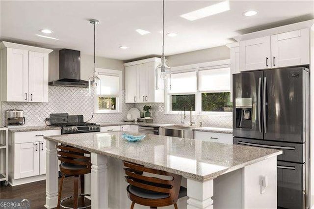 kitchen with stove, refrigerator with ice dispenser, white cabinets, a center island, and wall chimney exhaust hood