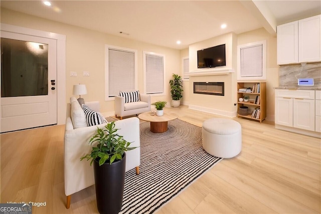 living area with recessed lighting, light wood-type flooring, and a glass covered fireplace