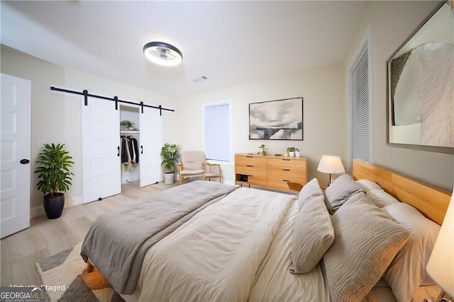 bedroom with wood finished floors, a closet, visible vents, and a barn door