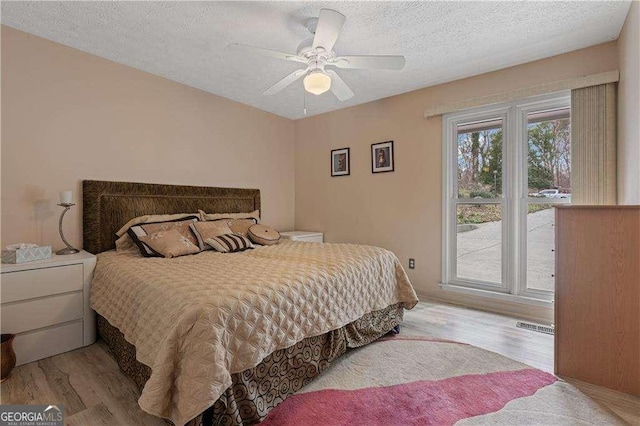 bedroom featuring ceiling fan, a textured ceiling, visible vents, and wood finished floors