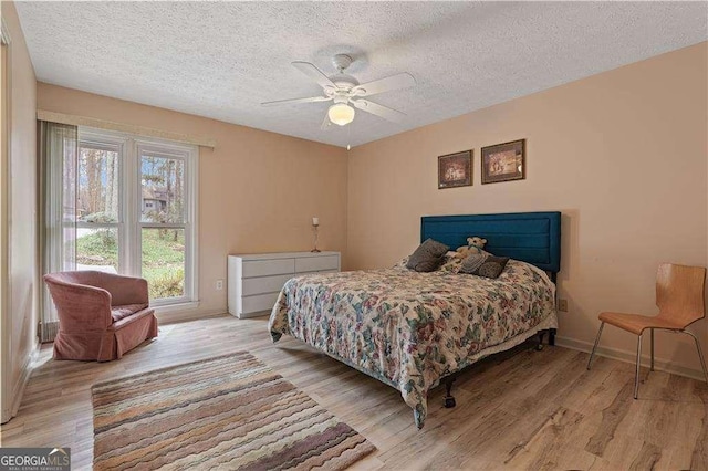 bedroom featuring a ceiling fan, a textured ceiling, baseboards, and wood finished floors