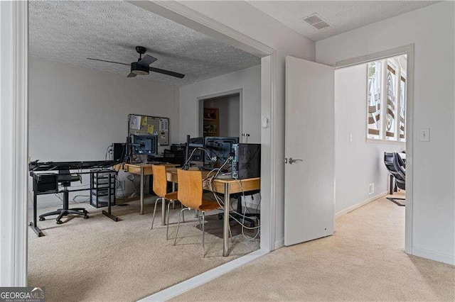 carpeted home office featuring a textured ceiling, baseboards, visible vents, and a ceiling fan