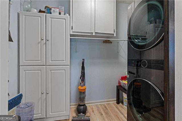 washroom with stacked washer and dryer, light wood-style flooring, and cabinet space