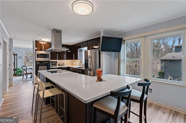 kitchen featuring light wood-style floors, a breakfast bar, island exhaust hood, light countertops, and black appliances