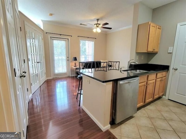 kitchen featuring dark countertops, stainless steel dishwasher, ornamental molding, a sink, and a peninsula