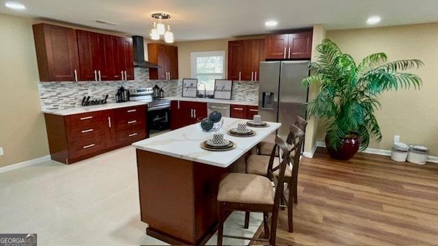 kitchen with tasteful backsplash, appliances with stainless steel finishes, a breakfast bar area, and wall chimney exhaust hood