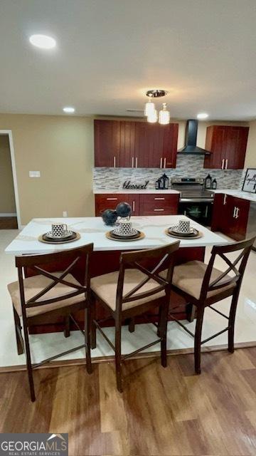 kitchen featuring light wood finished floors, backsplash, wall chimney exhaust hood, light countertops, and stainless steel electric range oven