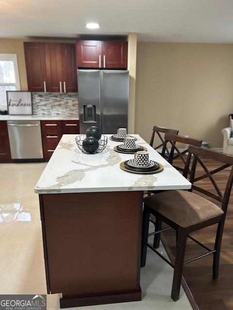 kitchen with tasteful backsplash, dark brown cabinets, light stone countertops, a kitchen breakfast bar, and stainless steel appliances