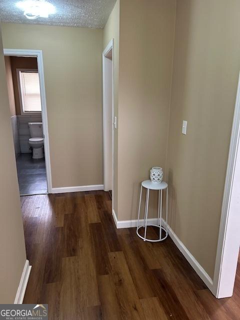 hallway with wood finished floors, baseboards, and a textured ceiling