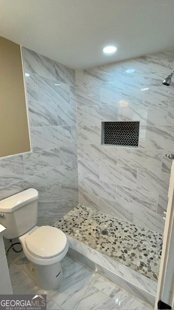 full bath featuring tiled shower, toilet, marble finish floor, and vanity