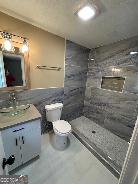 bathroom with tile walls, toilet, vanity, a tile shower, and a textured ceiling